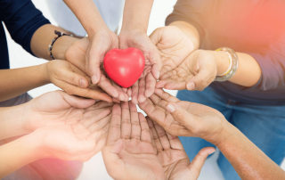 Photo of hands clasping together, holding up a love heart